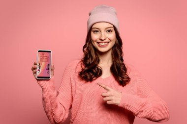 Parmakla akıllı telefonu gösteren mutlu bir kız. Ekrandaki en iyi alışveriş uygulaması. Pembe üzerine izole edilmiş.
