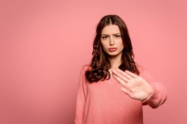 displeased girl showing stop gesture while looking at camera isolated on pink clipart
