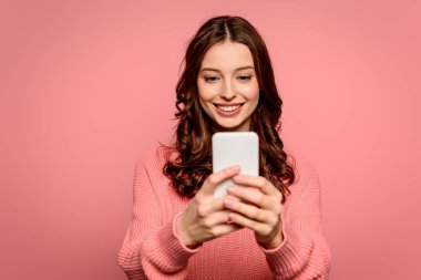 Mutlu kız, pembe telefonda görüntülü konuşma yaparken gülümsüyor.