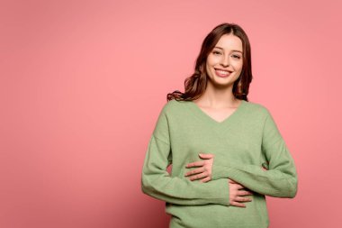 excited girl laughing while holding hands on stomach on pink background clipart