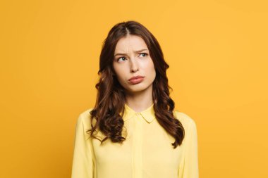 thoughtful, frowning girl looking away isolated on yellow clipart