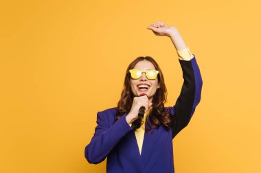 young singer in yellow glasses singing with raised hand isolated on yellow clipart