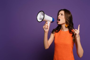 excited girl screaming in megaphone and showing attention gesture on purple background clipart