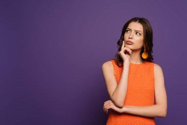thoughtful girl looking away while touching face on purple background clipart
