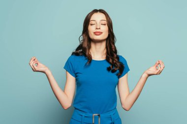 Gülümseyen kız meditasyon pozunda dikiliyor mavi arka planda gözleri kapalı