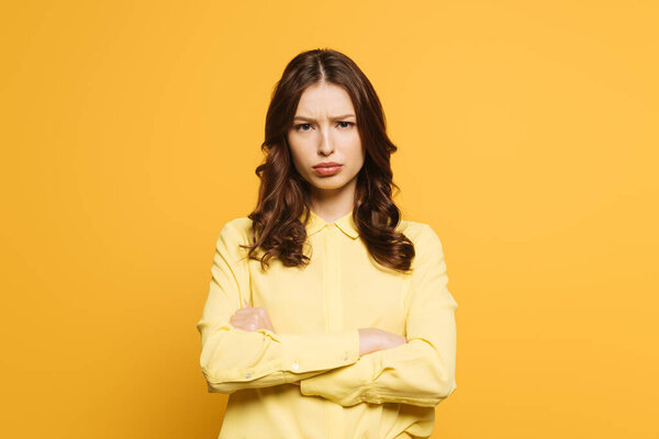 обиженная девушка, стоящая со скрещенными руками, глядя на камеру, изолированную на желтый

