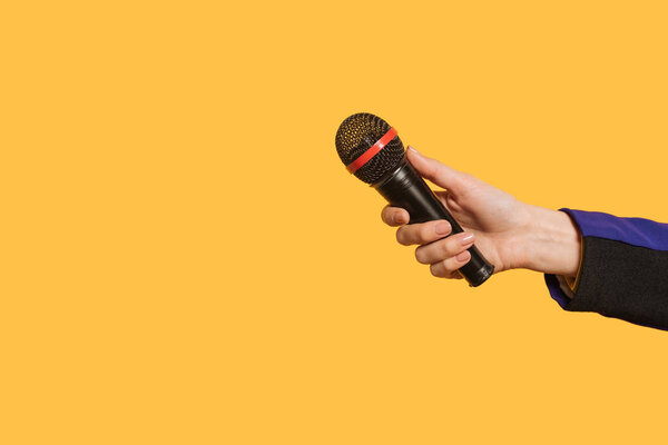 partial view of journalist holding microphone isolated on yellow