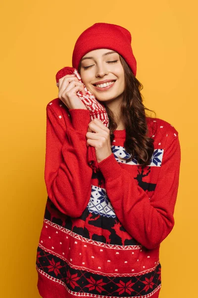 幸せな女の子で帽子と赤装飾セーター保持ミトン顔の近くに閉じられた目で単離された黄色 — ストック写真