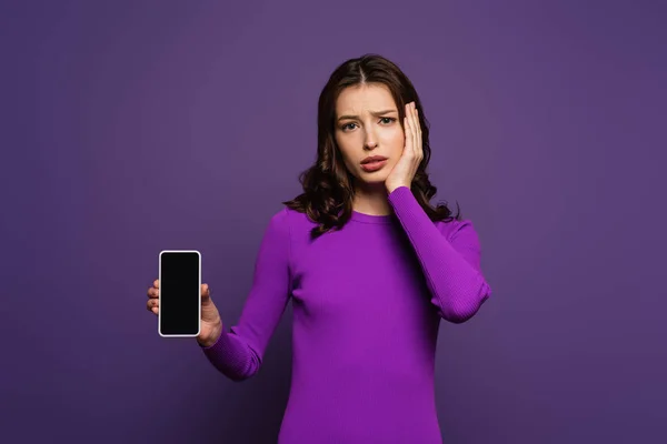紫の背景にスマートフォンを見せる動揺した女の子 — ストック写真