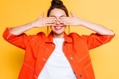 smiling girl covering eyes with hands on yellow background clipart