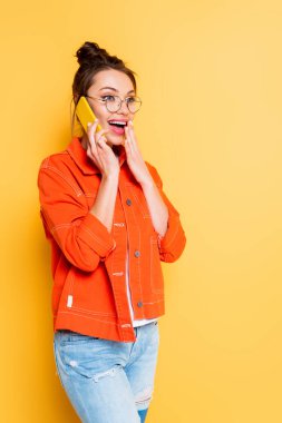 Sarı arka planda el ele tutuşurken akıllı telefondan konuşan heyecanlı öğrenci.