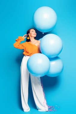 Mavi arka planda büyük şenlik balonları olan mutlu, modaya uygun bir kadın manzarası.