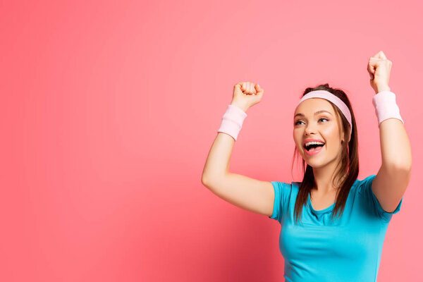 excited sportswoman showing winner gesture while looking away on pink background