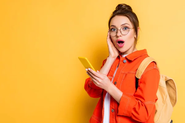 Shocked Student Eyeglasses Touching Face While Chatting Smartphone Yellow Background — Stock Photo, Image