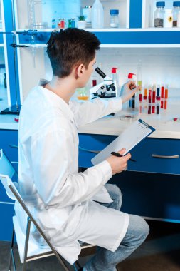 Beyaz önlüklü bilim adamı pano tutuyor ve test tüpüne dokunuyor. 