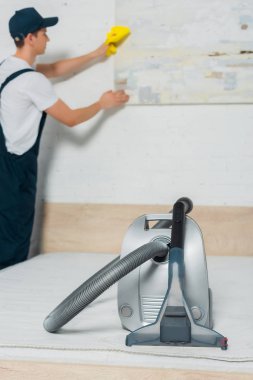 Üniformalı temizlikçi adamın yanında vakumun seçici odak noktası. 