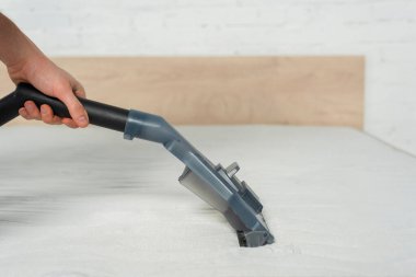 cropped view of cleaner removing dust on mattress in bedroom with vacuum cleaner  clipart