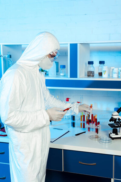 scientist in latex gloves holding syringe and test tube with coronavirus lettering 