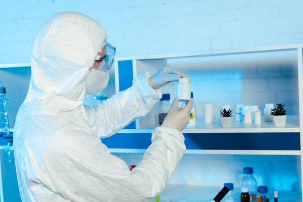 scientist in latex gloves and goggles looking at bottle in laboratory 