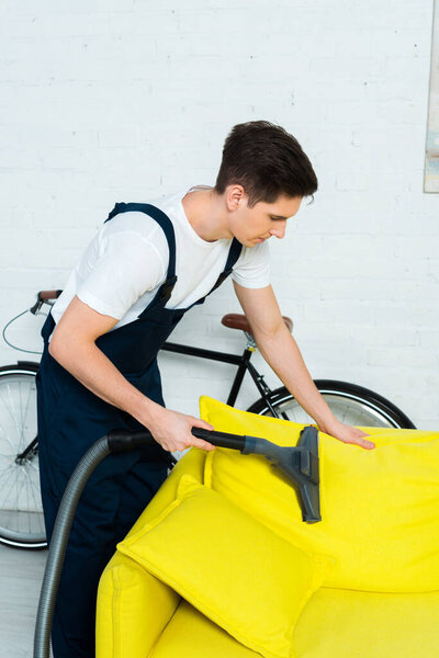 handsome cleaner in overalls dry cleaning sofa with vacuum cleaner 