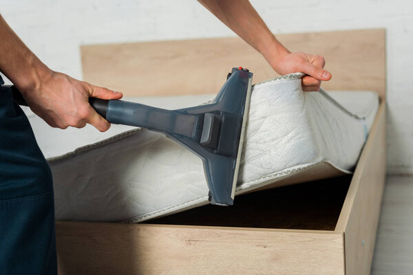 cropped view of man removing dust on mattress with vacuum cleaner 