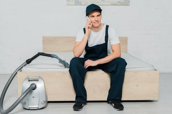Happy Cleaner Cap Sitting Bed Talking Smartphone Vacuum Cleaner — Stock Photo, Image