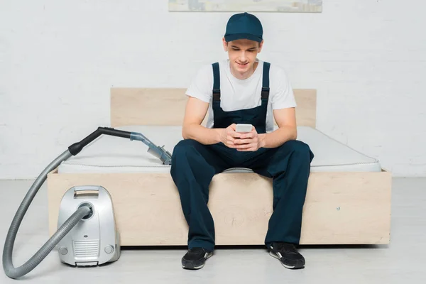 Happy Cleaner Cap Sitting Bed Using Smartphone Vacuum Cleaner — Stock Photo, Image