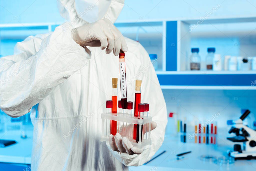 cropped view of scientist in hazmat suit and latex gloves holding test tube with coronavirus lettering 