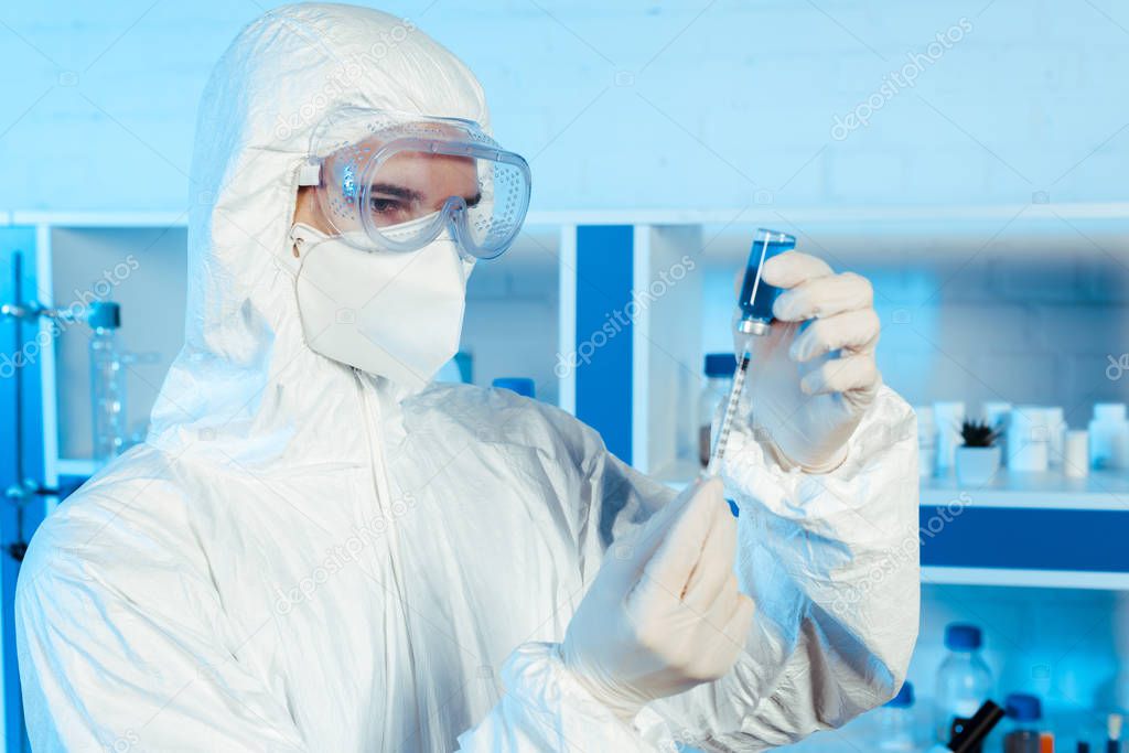 scientist in hazmat suit holding syringe and bottle with vaccine 