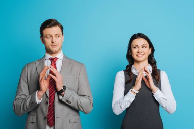 smiling, cunning businessman and businesswoman holding joined fingers on blue background clipart