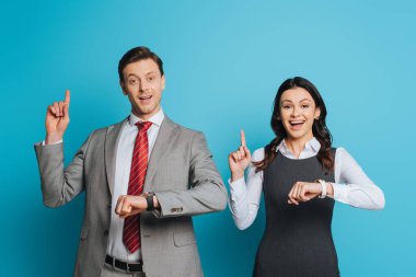 Mavi arka plandaki kameraya bakarken fikir belirtileri gösteren iki gülümseyen iş adamı.