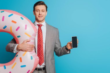 Yüzme yüzüklü gülümseyen iş adamı mavi arka planda boş ekranlı akıllı telefonu gösteriyor