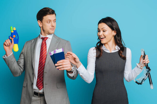 smiling businessman holding passports and air tickets near cheerful businesswoman with diving mask on blue background