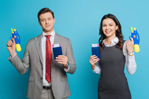 two excited businesspeople holding passports, air tickets and water guns on blue background