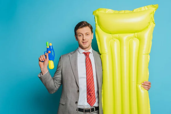Smiling Businessman Holding Inflatable Mattress Water Gun Blue Background — Stock Photo, Image