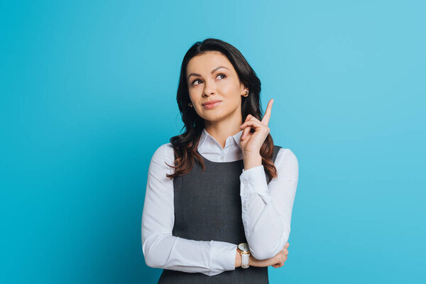 dreamy businesswoman looking up while showing idea gesture on blue background