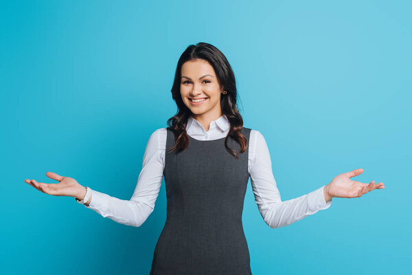 happy businesswoman smiling at camera while standing with open arms on blue background