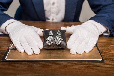 Mücevher eksperi, mücevher kazancını mücevher yastığının üzerinde gri masanın yanındaki masada tutuyor.