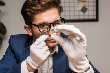 Jewelry appraiser with magnifying glass examining gemstone in workshop clipart