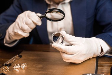 Mücevher eksperi, mücevher yüzüklerinin yanında mücevher ve büyüteç tutuyor.