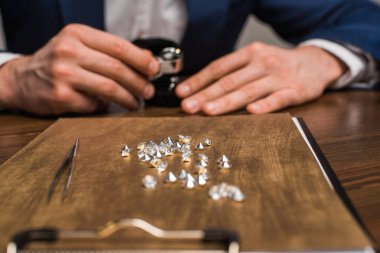 Mücevherlerin seçici odak noktası tahtada ve mücevher değer biçme uzmanı gri masada izole edilmiş.