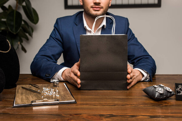Cropped view of jewelry appraiser holding paper bag near jewelry on table in workshop