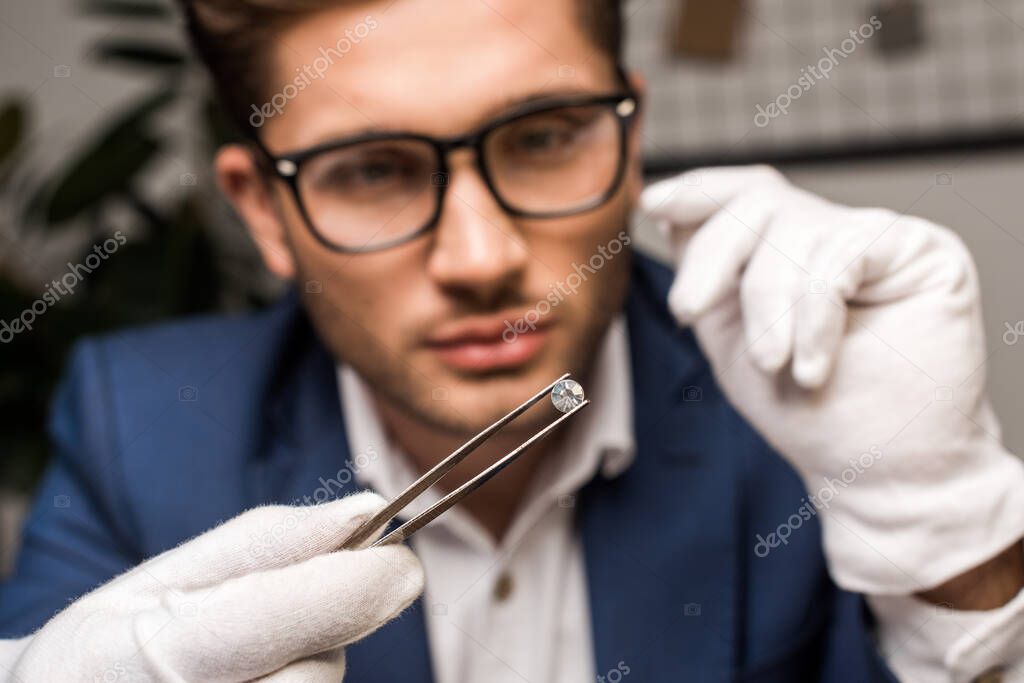 Selective focus of jewelry appraiser holding gemstone in tweezers while working in workshop 