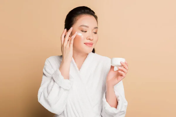 Smiling Beautiful Asian Woman Bathrobe Applying Face Cream Beige Background — Stock Photo, Image