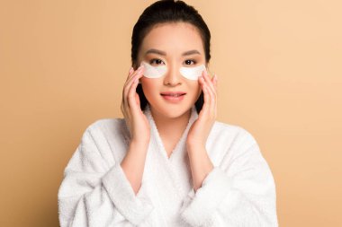 beautiful asian woman in bathrobe with eye patches on face on beige background clipart