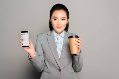 KYIV, UKRAINE -  FEBRUARY 11, 2019: happy young businesswoman with paper cup holding smartphone with apple music app on grey background