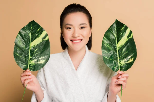幸せな美しいアジア人女性でバスローブに緑の葉でベージュ — ストック写真