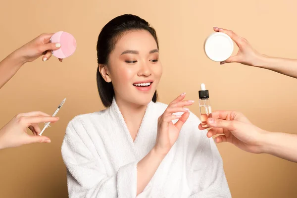 用面部清洁刷 注射器 化妆品霜和米色背景的油 在靠近双手的浴衣中微笑美丽的亚洲女人 — 图库照片