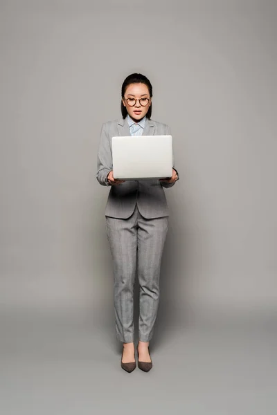 眼鏡の若い実業家がグレーの背景にノートパソコンを使って — ストック写真