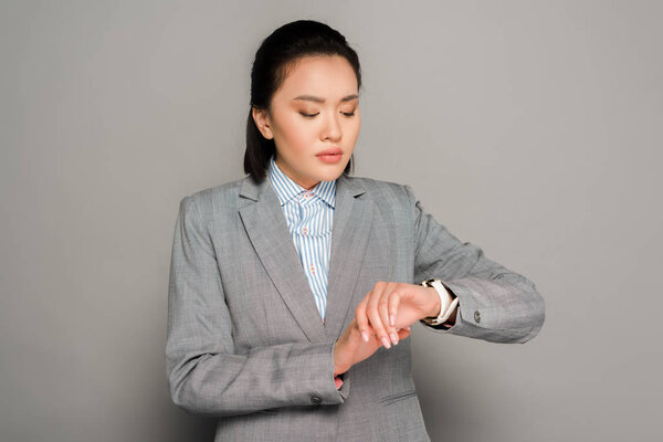 young businesswoman in suit looking at wristwatch on grey background